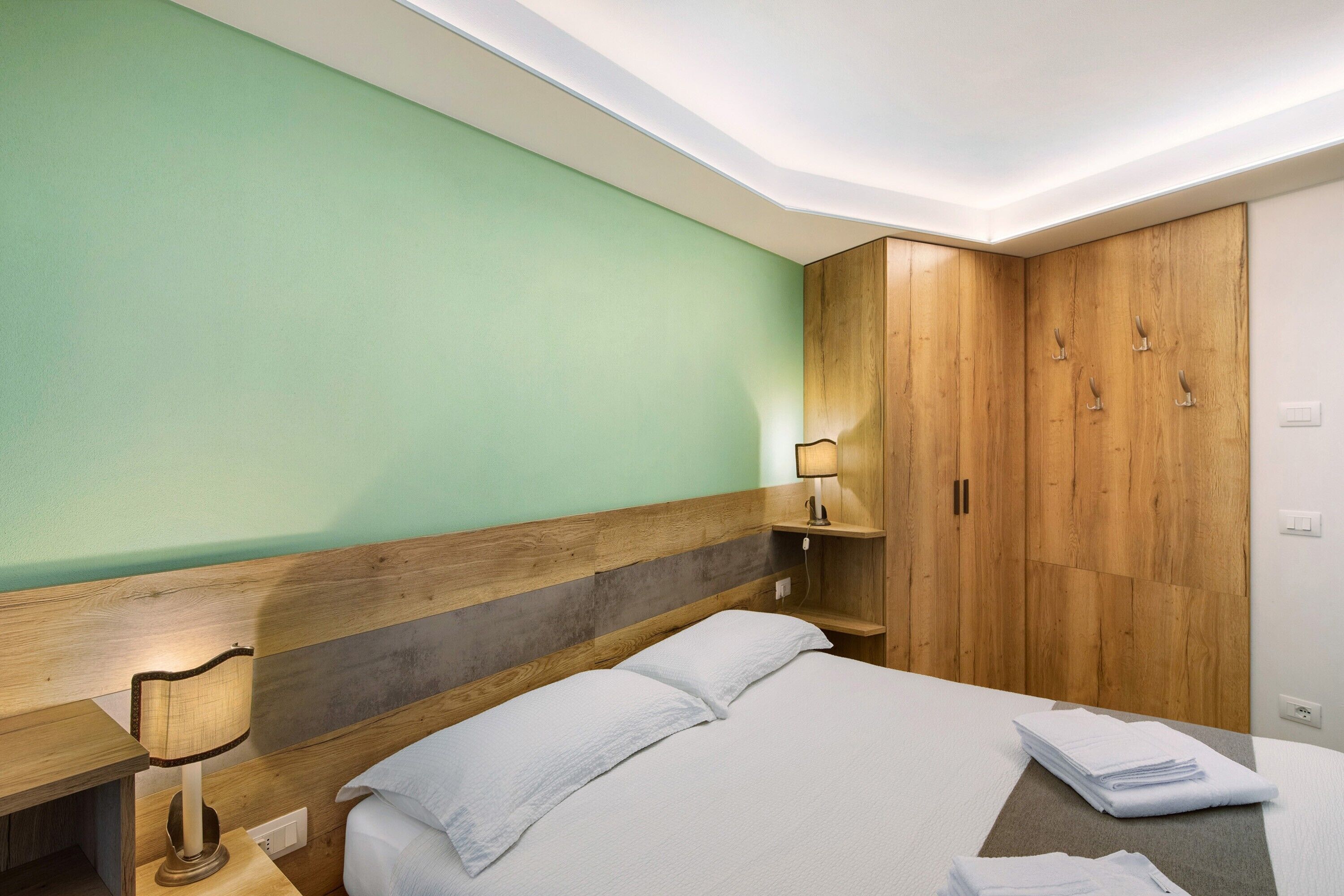 Ein Hotelzimmer mit Bett, Holzschrank, Nachttischlampe und grüner Wand.