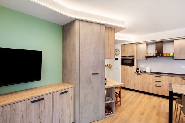A modern kitchen with wooden cabinets, a flat-screen TV, and a dining area.