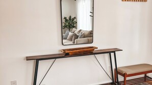 Een kamer met een houten console, een bankje, een grote spiegel en een kamerbreed tapijt.