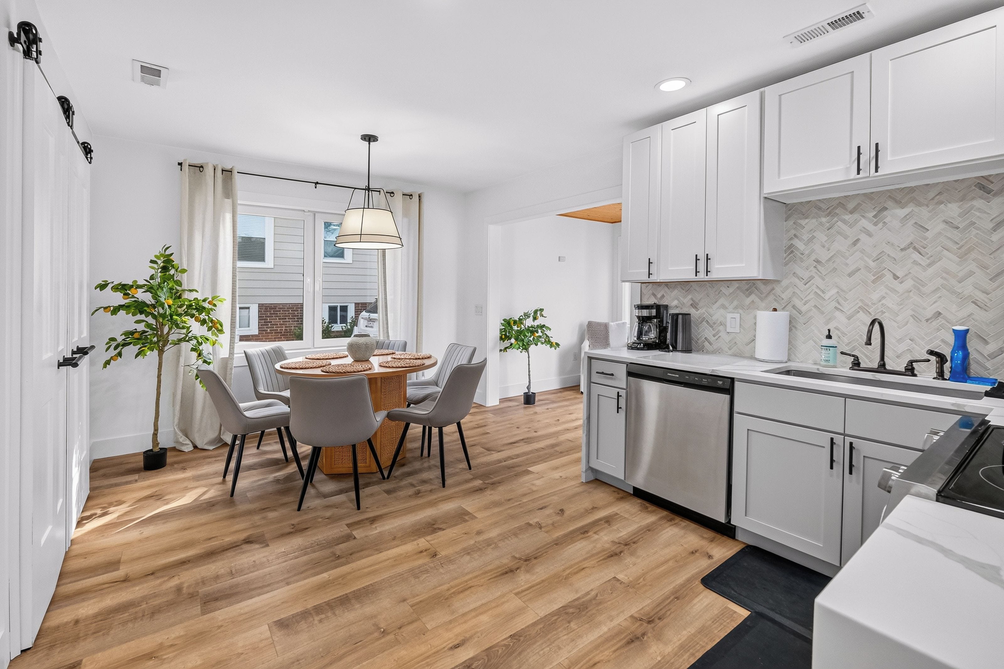 A modern kitchen with white cabinets, a built-in dishwasher, and a dining area with a round table and chairs.
