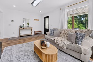 A modern living room with a sofa, coffee table, and a view of greenery outside.