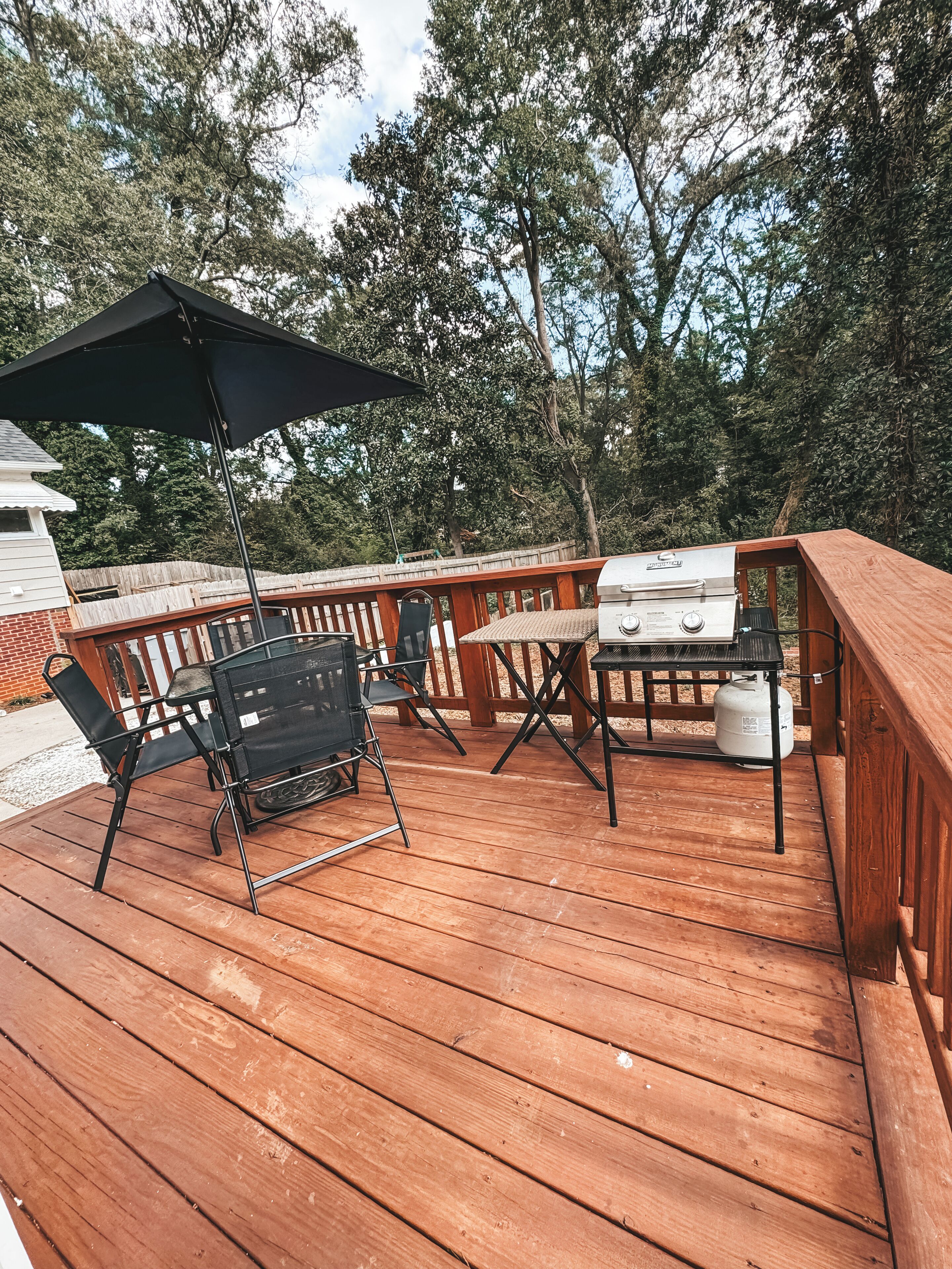 A wooden deck with a grill, chairs, and an umbrella.