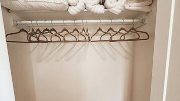 A closet with a wooden floor, a hanging rod with clothes, and rolled-up towels on the top shelf.