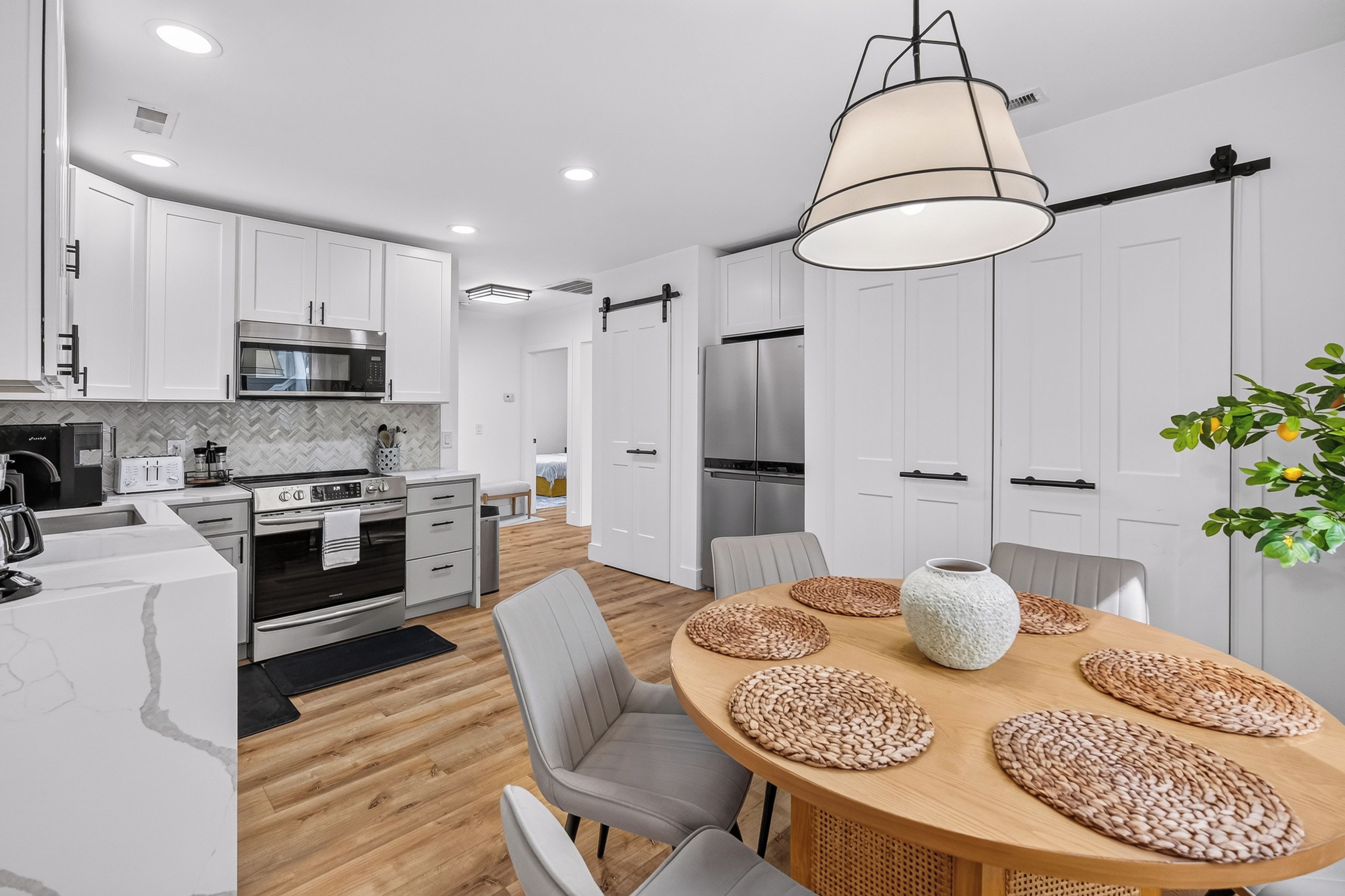 A modern kitchen with white cabinetry, stainless steel appliances, and a wooden dining table with woven placemats.
