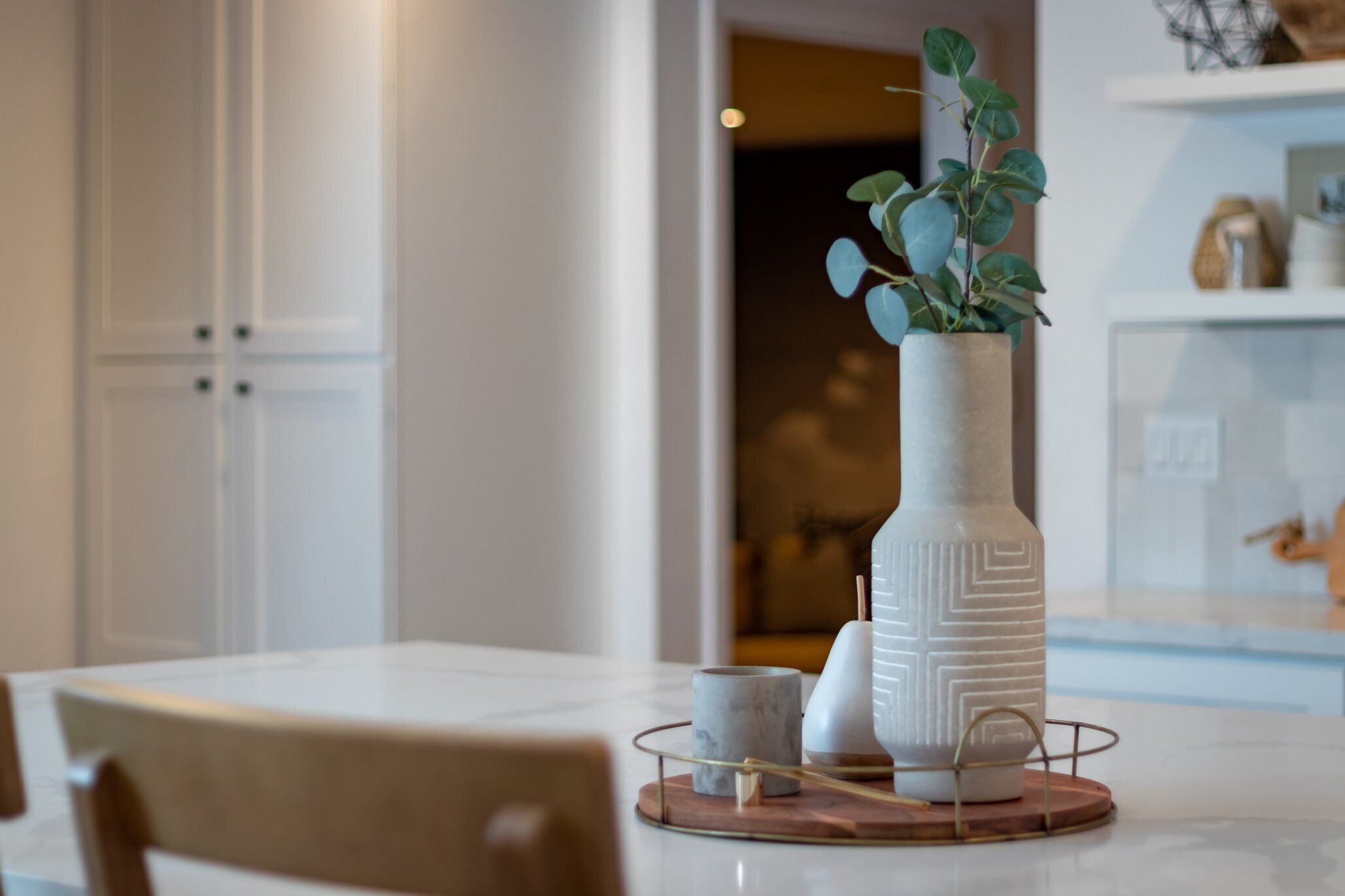 Una cuina moderna amb armaris blancs, un taulell de marbre i un gerro decoratiu amb una planta.