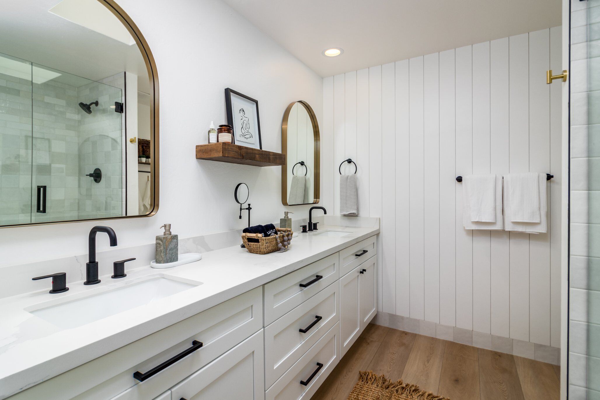 A modern bathroom with a white vanity, a glass shower enclosure, and a wooden floor.