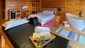 Une pièce chaleureuse aménagée dans une cabane en bois, avec un lit, un petit bureau, une coiffeuse avec un miroir et une baignoire.