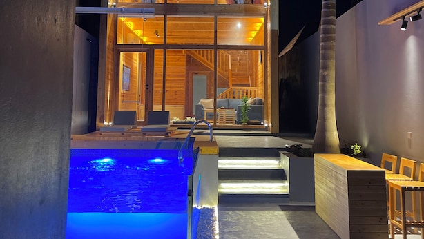 Une maison moderne en bois, dotée d’une piscine, d’un espace salon extérieur et d’un escalier menant à l’entrée.