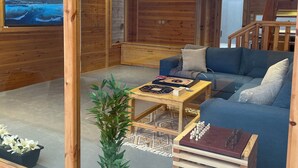 L'intérieur d'un chalet moderne en bois, avec une grande porte vitrée, un canapé bleu, une table basse en bois et une petite plante.