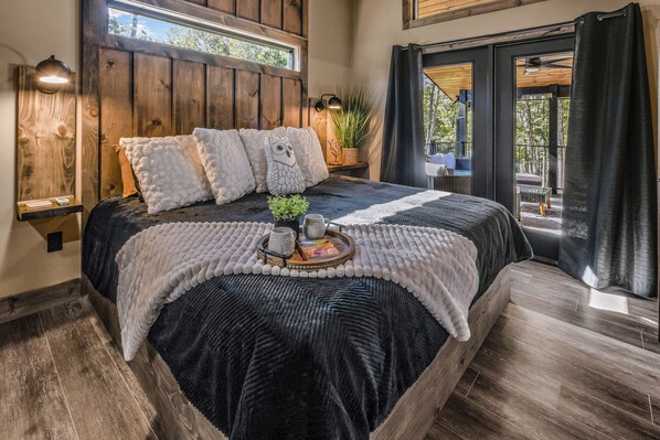 A bedroom with a large bed, wooden headboard, a bedside table with a lamp, and a view of the outdoors through a glass door.