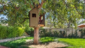A treehouse with a wooden exterior and a small window, surrounded by lush greenery and a stone wall. - Updated Spacious 4-bedroom house near Nob Hill and UNM.  (Albuquerque)