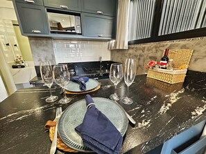 A kitchen with a dark marble countertop, a built-in microwave, and a wicker basket with a bottle and snacks. - Loft for a House in Bombinhas - NO GARAGE (Centro Bombinhas)