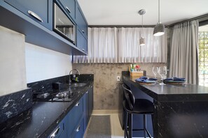 Eine moderne Küche mit dunkelblauen Schränken, einer schwarzen Arbeitsplatte und einem eingebauten Herd. Es gibt eine Bar mit Hockern und eine kleine Kücheninsel mit Spüle und Barbeware.