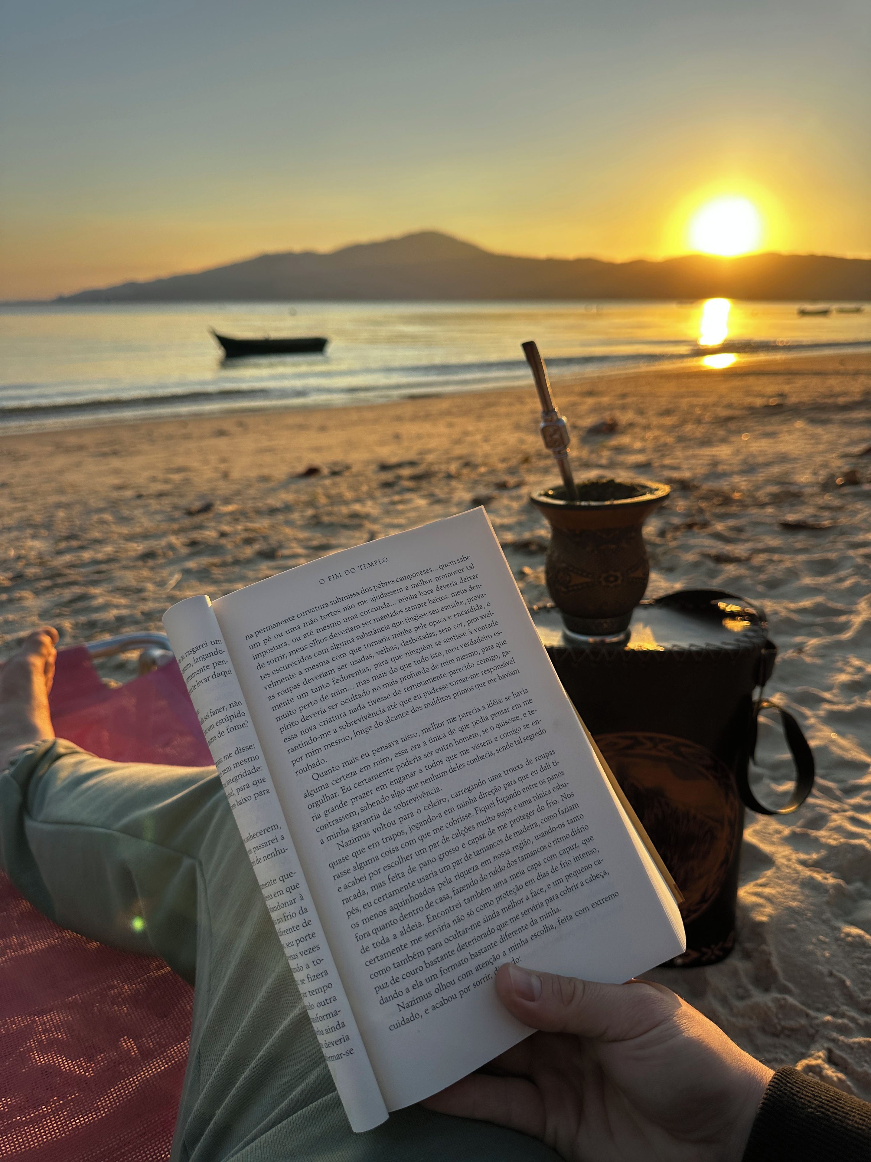 A person reading a book on a beach with a sunset in the background.