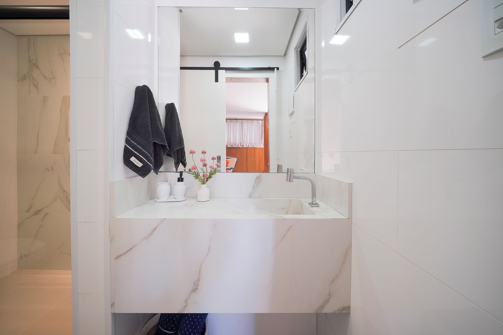 Une salle de bain moderne avec un lavabo en marbre blanc, un miroir et deux serviettes suspendues à un porte-serviettes.