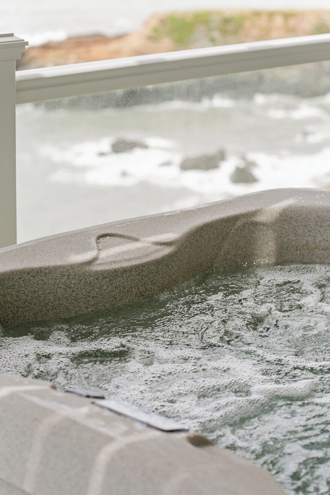 A stone bathtub with a textured surface, a visible drain, and a view of a body of water outside.