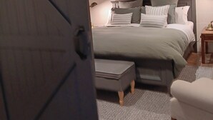 A bedroom with a bed, a nightstand, a chair, and a painting on the wall.
