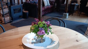 A wooden dining table with a white plate and a glass vase of purple flowers.