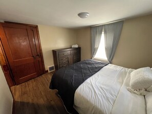 Cozy retreat with a comfortable bed, dresser, and window with sheer curtains.