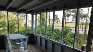 Eine überdachte Veranda mit Tisch und Stühlen, großen Fenstern und Blick auf einen See und grüne Vegetation.