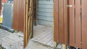 Eine Holzdielen-Terrasse mit Metallgeländer, einer Schiebeglastür und einem kleinen Außenbereich mit Fliesenboden.