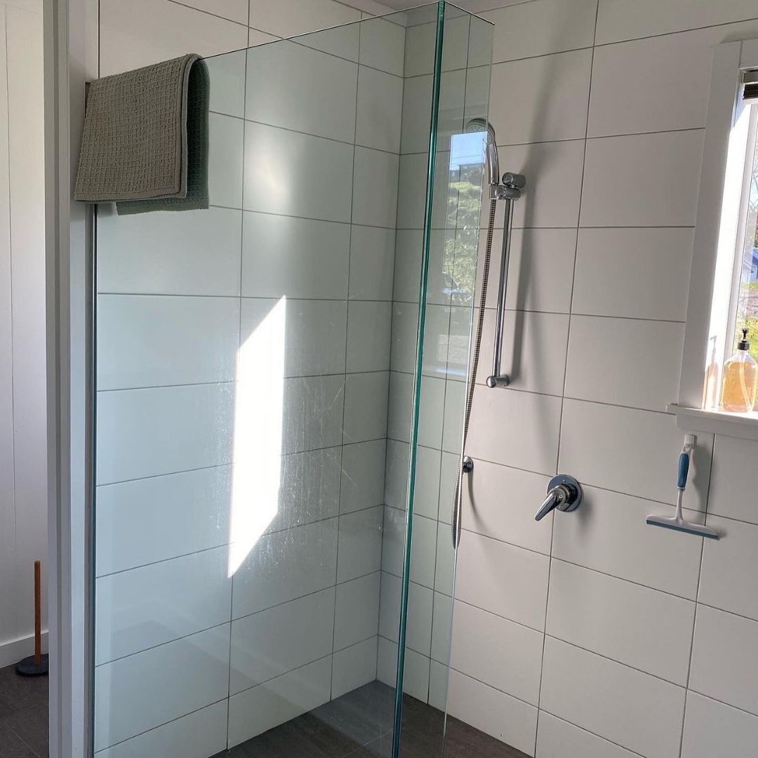 Une douche fermée par des parois en verre, dotée d’un pommeau de douche à main et d’un distributeur de savon à main.