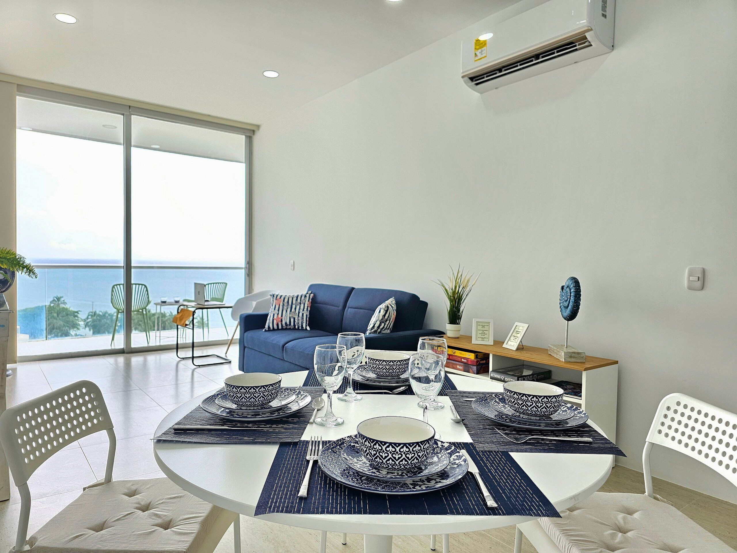 Un moderno comedor con una mesa redonda preparada para cuatro personas, con vajilla blanca y azul estampada.