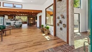 A spacious living area with a wooden floor, a stone accent wall, and a large window providing natural light. - Los Sueños Ranch Elgin AZ  (Elgin)