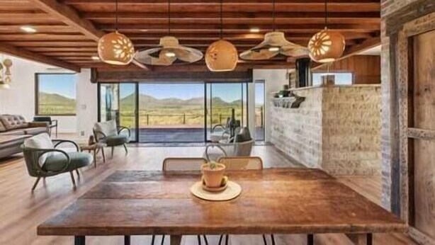 A spacious dining area with a wooden table, chairs, and a view of the mountains through large windows. - Los Sueños Ranch Elgin AZ  (Elgin)