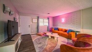 Una sala de estar con televisor, sofá naranja y alfombra estampada.