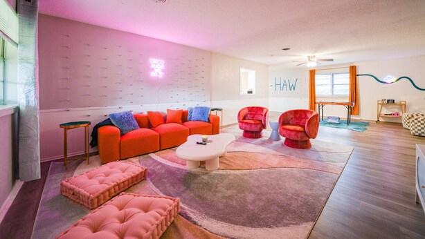 Una sala de estar moderna con un sofá rojo, una mesa de centro blanca y un otoman rosado.