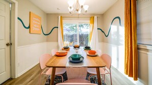 Comedor con mesa de madera, sillas rosadas y una lámpara de araña.