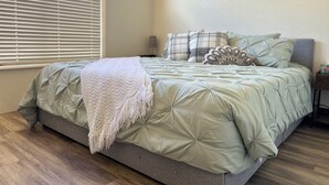 Ein Schlafzimmer mit einem Bett, einem Fenster mit Jalousien und zwei an der Wand befestigten Blumenbildern.