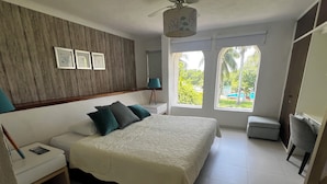 Une chambre à coucher comprenant un lit, des tables de chevet, une commode, un ventilateur de plafond et une fenêtre donnant sur un paysage verdoyant.