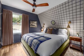 A bedroom with a bed, curtains, a ceiling fan, a nightstand, a lamp, and a wall clock. - Frog Hollow · A-Frame & Hot Tub · Stay with Branch (Berkeley Springs)
