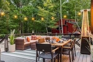 An outdoor deck with a dining area, a sofa, and a grill. - Frog Hollow · A-Frame & Hot Tub · Stay with Branch (Berkeley Springs)
