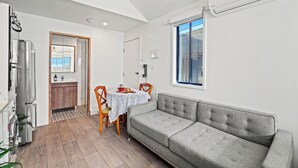 Une cuisine moderne dotée d’un four et d’un réfrigérateur encastrés, un coin repas avec une table et des chaises, et un canapé gris dans une pi èce lumineuse avec une grande fenêtre.
