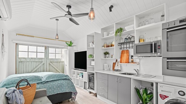 Un appartement moderne et compact, doté d’une kitchenette, d’un téléviseur à écran plat et d’un lit recouvert d’une couvre-lit à motifs bleus et blancs.