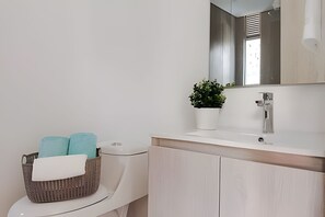 A modern bathroom with a toilet, a sink, a mirror, and a potted plant.