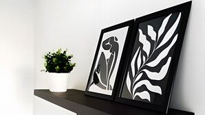 Uma prateleira de madeira escura com duas obras de arte emolduradas em preto e branco e um vaso com planta.