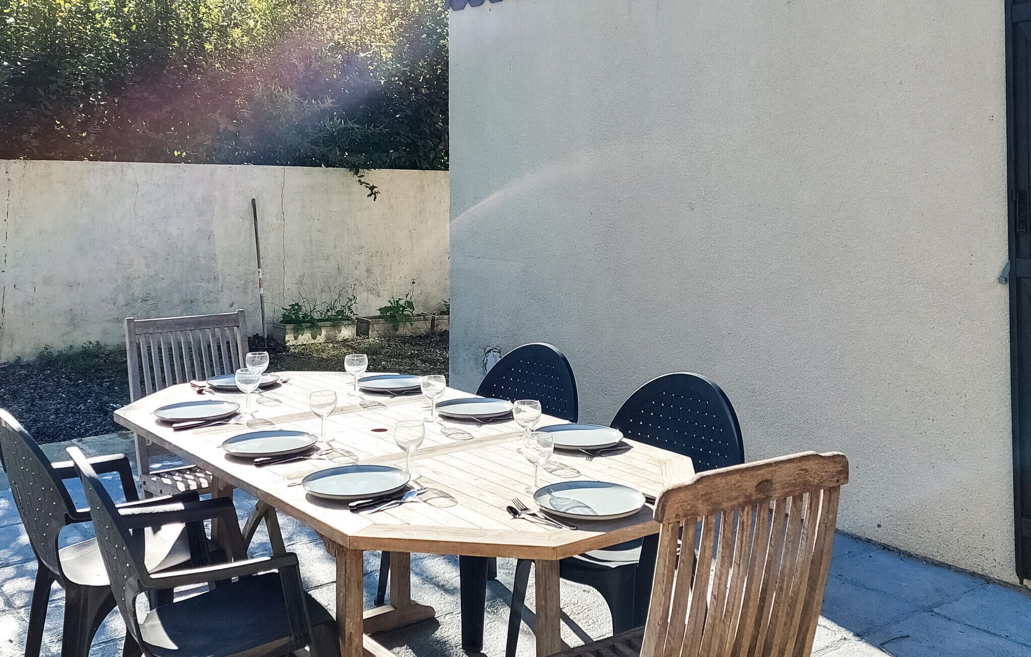 Uma área de refeições ao ar livre com uma mesa de madeira posta para seis pessoas, cercada por cadeiras pretas.