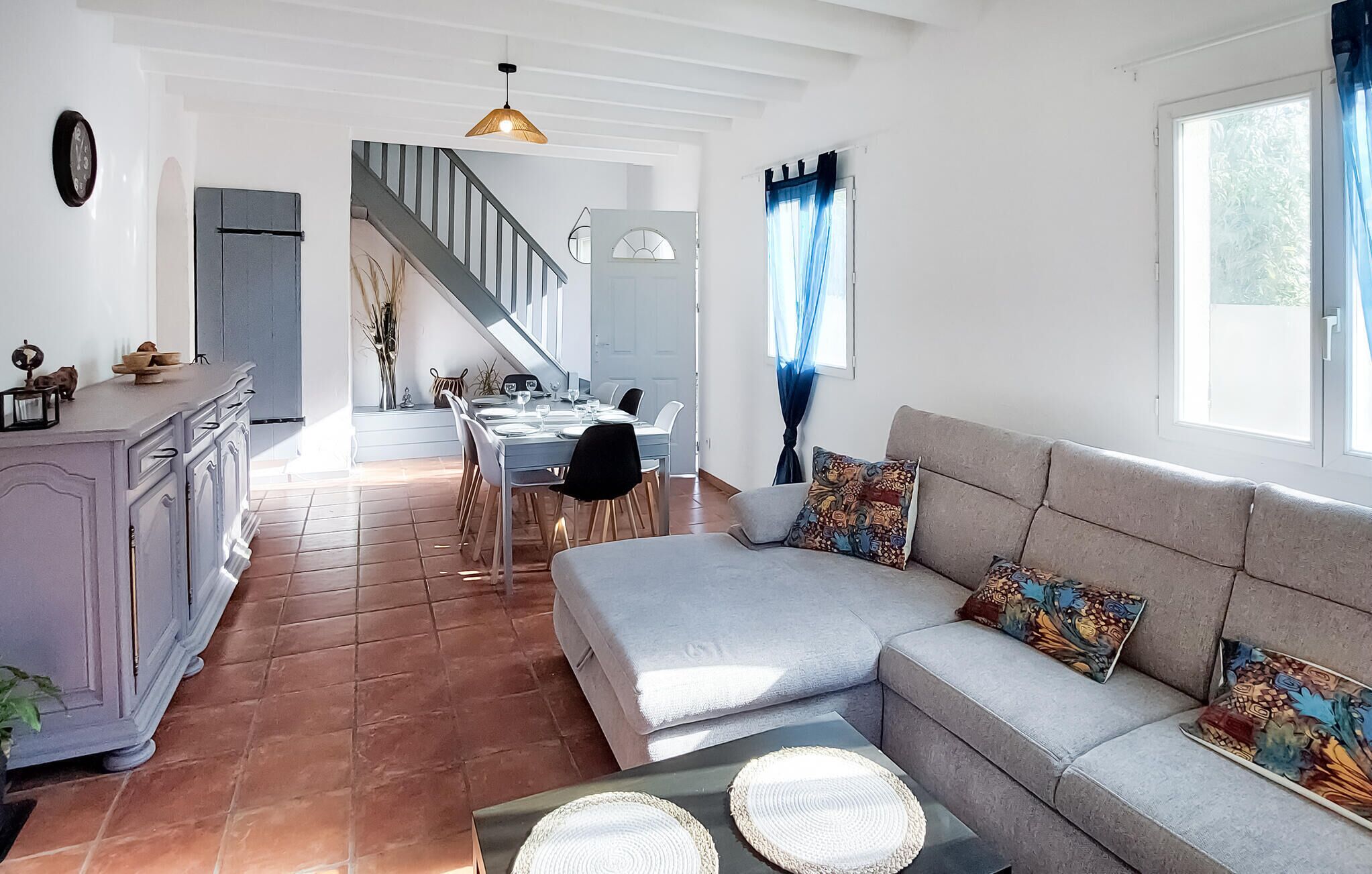 Een ruime woonkamer met een bank, een eettafel en een keukenhoek met een trap.