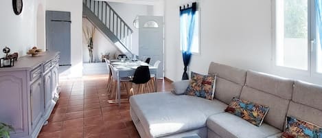 A spacious living area with a sofa, a dining table, and a kitchen area with a staircase.