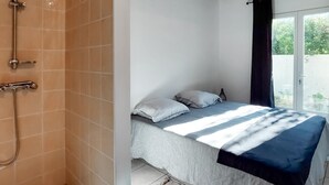 Ein Schlafzimmer mit einem Bett, Kissen, einem Fenster mit Vorhängen und einer Duschkabine mit Duschkopf.