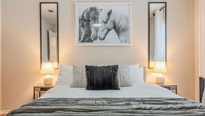 A neatly made bed with a black throw blanket, two bedside lamps, and a framed picture of horses on the wall.