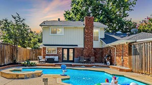A two-story house with a backyard swimming pool, a brick chimney, and a fenced area with outdoor furniture.