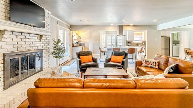 A living room with a fireplace, leather sofas, and a dining area in the background.
