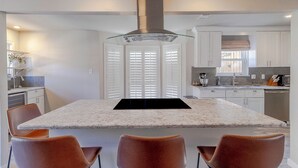 A modern kitchen with a central island, white cabinetry, and a stainless steel range hood.