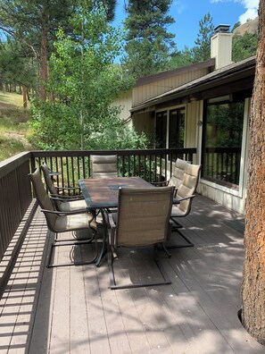 Eine Holzterrasse mit Tisch und Stühlen, umgeben von einer Brüstung und Bäumen.