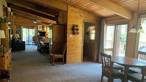 A cozy cabin interior with a wooden interior, a dining area with chairs and a table, and a kitchen visible through an open door.